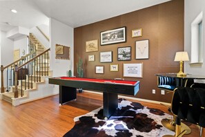 The living room features a game table and a mini bar table with seating for two