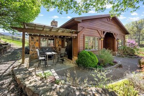 Shaded patio with grill and outdoor dining under a wooden pergola.
