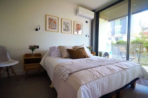Relax in this cozy bedroom featuring a queen-sized bed, beautiful artwork, and a lovely balcony view for a perfect getaway.