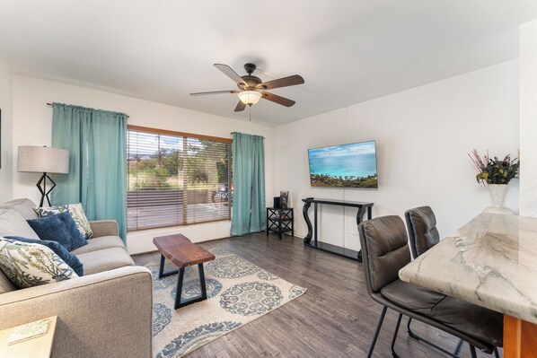 Cozy living room with sleeper sofa, smart TV, A/C, and large windows for natural light.