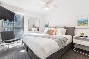 Recharge in the primary bedroom, complete with a king bed, wall-mounted TV, ceiling fan, and blackout blinds — all designed for a peaceful night’s sleep.