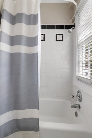 Cozy Bathroom Retreat – Enjoy a relaxing soak in this charming tub surrounded by natural light and classic black-and-white tiling.