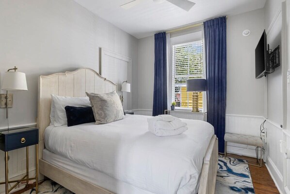 A serene bedroom featuring plush bedding, calming tones, and abundant natural light through tall windows.