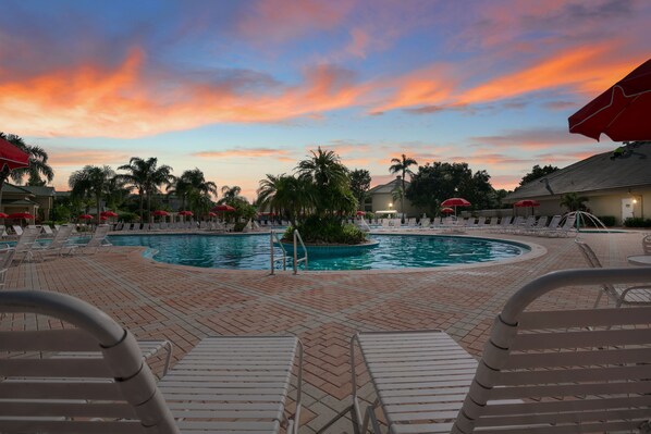 Dive into relaxation at the stunning outdoor pool surrounded by palm trees and lounge chairs, set against a beautiful sunset backdrop.