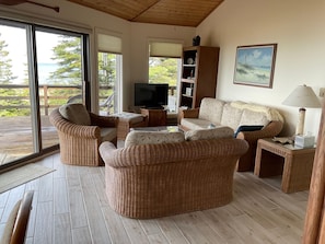 Cozy living space with wicker furniture, lake-facing views, and direct access to the spacious wraparound deck.