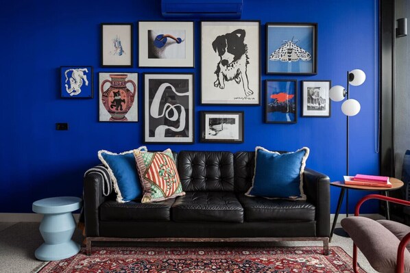 Lounge in style in this vibrant living room, featuring a bold blue wall, eclectic artwork, and a sleek leather sofa that adds a modern touch to the space