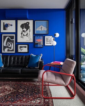 This vibrant living room features a bold blue accent wall, curated gallery art, designer furniture, and large windows that fill the space with natural light