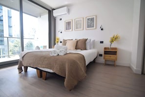 Bright and airy bedroom with large windows, cozy linens, and minimalist decor, perfect for a relaxing stay.