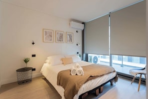 Relax in this modern bedroom featuring a cozy queen bed, stylish decor, and ample natural light for a refreshing stay.