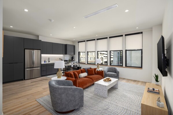 Sophisticated comfort—this open-concept living space blends the modern kitchen and cozy living room, bathed in natural light from expansive windows overlooking the city.