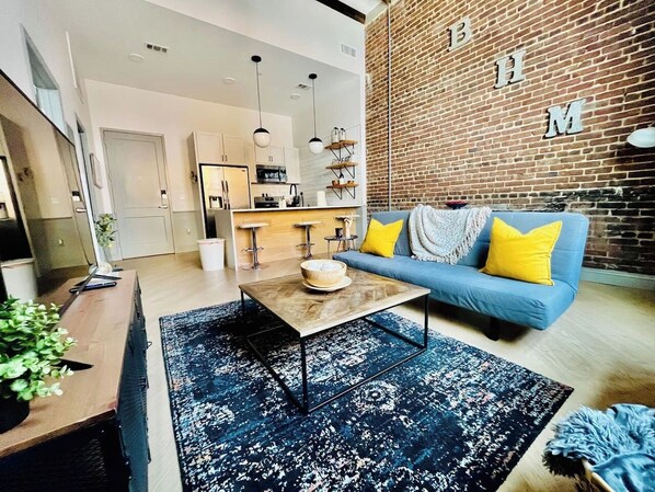 Experience comfort & style in this cozy living room inside the historic Mercantile building on Morris Ave. Fully equipped kitchen, modern decor, and access to amenities. *please note that we have a new sofa, it is no longer a sleeper sofa*