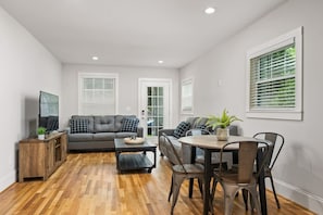 Spacious and bright, the combined living and dining space features contemporary furnishings, large windows that flood the room with natural light, and a dining table set for four.