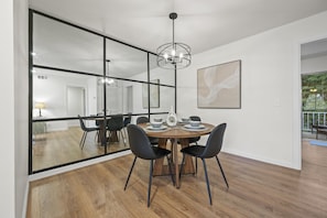 This inviting dining room features a chic table for four, perfect for intimate meals. A mirrored wall reflects natural light, creating an open, airy feel. Elegant decor and comfortable seating complete the space, ideal for cozy dinners or relaxed brunches.