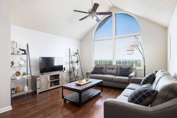 Welcome to Unit G!! A spacious living room with a gray sectional, vaulted ceilings, and queen pull-out bed greet you for your stay at your home away from home.