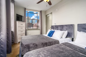 Stylish bedroom with two queen beds, large windows, fresh linens, and vibrant accent pillows.
