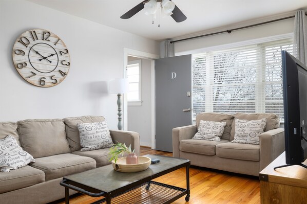 Welcome to Unit D at Vulcan View!! Bright and airy living room in Unit D, featuring comfortable seating, a farmhouse clock, and large windows for natural light.