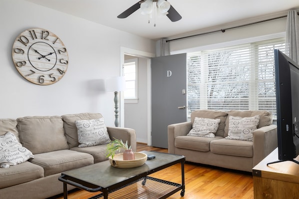 Welcome to Unit D at Vulcan View!! Bright and airy living room in Unit D, featuring comfortable seating, a farmhouse clock, and large windows for natural light.