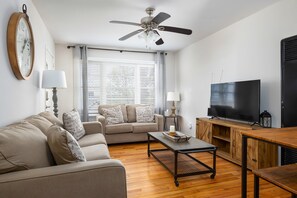 Unit B's living room mirrors the inviting design of Unit A, with soft beige couches, a smart TV, and a warm, welcoming atmosphere.