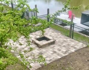Fenced in backyard with firepit next to waterfront and dock.