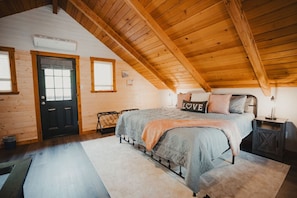 Loft Bedroom Retreat – Door to the exterior deck offers views of the firepit, creek & falls. A mini-split AC/Heat unit provides year-round comfort. Luggage racks, nightstands w/lighting options, USB chargers, & touch lamps add to the convenience.