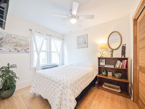 This inviting bedroom offers a serene atmosphere with a ceiling fan, smart TV, and a beautifully organized bookshelf, ideal for family downtime.