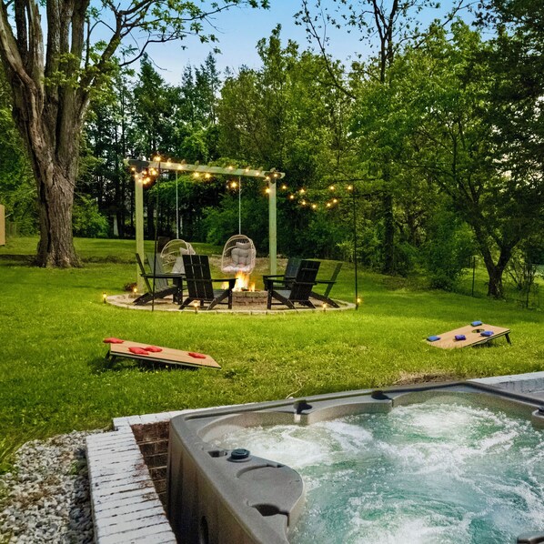 Outdoor games, fire pit area, hot tub, patio area surrounded by greenery.