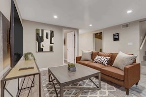 Relax in Style! Our Living Room Boasts a Cozy Sofa, Spacious Smart TV, Comfortable Chairs, Soft Lamps, Convenient Table, and Inviting Lighting.