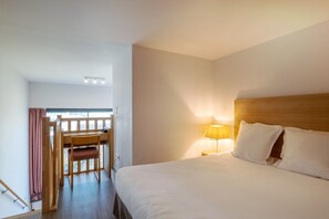 A serene bedroom featuring a comfortable bed and a small writing desk, illuminated by a warm lamp.
