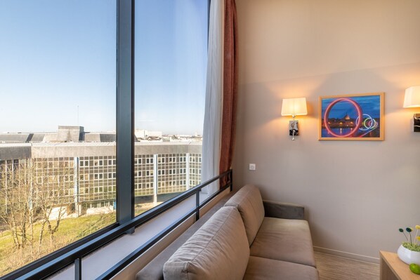 A cozy living area featuring a soft gray sofa beside a large window, offering a bright view of the outside.
