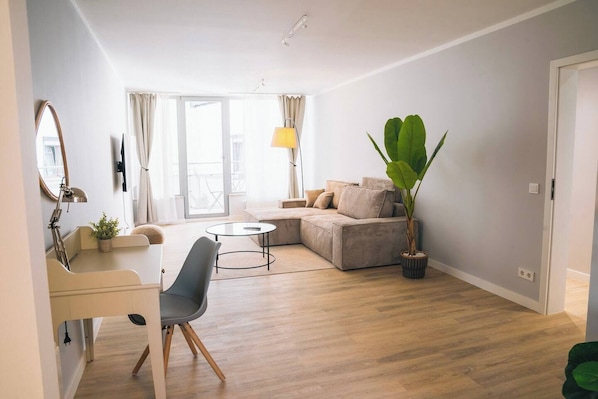 Spacious living room with large sofa bed, Smart TV, desk and balcony access.