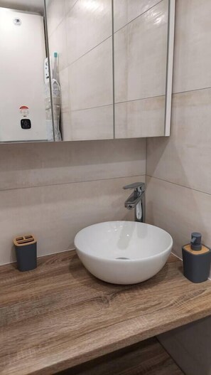 Vasque sur étagère / plan de travail surmontée d'une armoire de toilette, 2 spots indépendants au plafond et prise électrique sur la gauche..