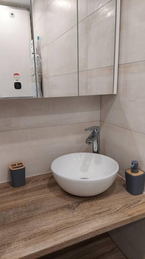 Vasque sur étagère / plan de travail surmontée d'une armoire de toilette, 2 spots indépendants au plafond et prise électrique sur la gauche..
