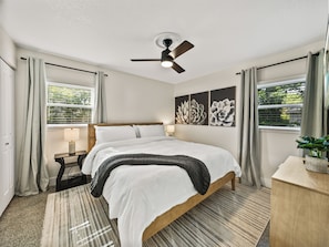 Spacious master bedroom with a king bed, warm earth-tone decor, and dual windows for natural light. Enjoy a mounted TV, blackout curtains, ceiling fan, and two closets—perfect for comfort and longer stays.