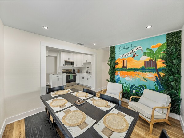 The modern dining area features sleek chairs and a minimalist table, perfect for comfort and connection. A striking mural by a local artist showcases Lakeland’s iconic lakes, landmarks, and downtown, adding a vibrant, personal touch.