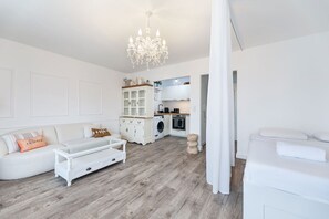Bright and airy studio view featuring a cozy lounge, elegant chandelier, and a modern open kitchen.