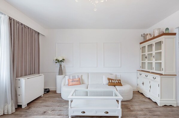 Chic and serene living room corner with a cozy boucle sofa, glass-top coffee table, and a classic hutch cabinet