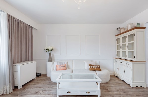Chic and serene living room corner with a cozy boucle sofa, glass-top coffee table, and a classic hutch cabinet