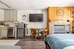 Cozy studio with kitchen, dining area, fireplace, TV, wood accents, and bed.
