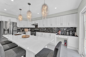 Bright kitchen with crystal lights, white cabinets, and sleek black backsplash.