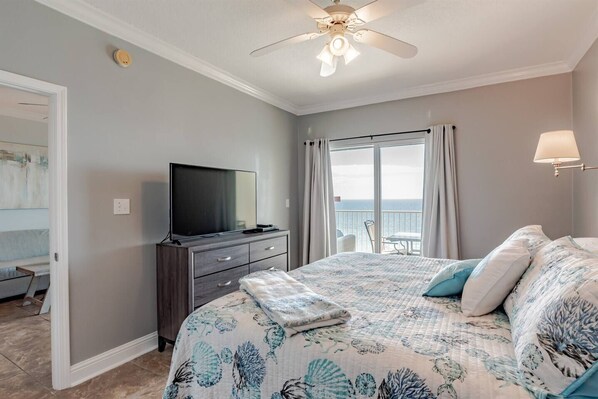 Master bedroom features sliding glass doors with access to balcony with beachfront ocean views. This bedroom is furnished with a king-sized bed, nightstands, dresser, large TV, closet, and access to the ensuite full bathroom.