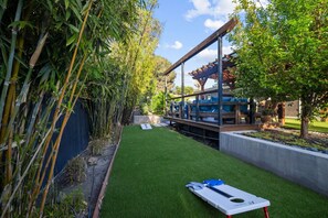 Private backyard with cornhole, lush landscaping, and a cozy lounge for relaxing after play.