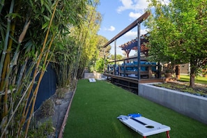 Private backyard with cornhole, lush landscaping, and a cozy lounge for relaxing after play.