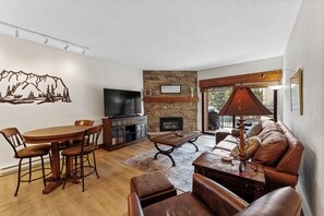 Living area with a large flat-screen TV, beautiful stone fireplace, queen sleeper sofa, and balcony access.