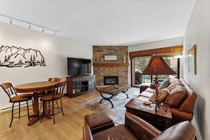 Living area with a large flat-screen TV, beautiful stone fireplace, queen sleeper sofa, and balcony access.