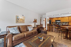Living area with a large flat-screen TV, beautiful stone fireplace, queen sleeper sofa, and balcony access.
