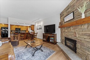 Living area with a large flat-screen TV, beautiful stone fireplace, queen sleeper sofa, and balcony access.