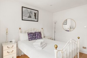 A bright and minimalistic bedroom featuring a white metal-frame bed, soft linens, and elegant black-and-white artwork for a peaceful, inviting retreat.