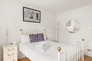A bright and minimalistic bedroom featuring a white metal-frame bed, soft linens, and elegant black-and-white artwork for a peaceful, inviting retreat.