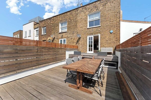 A spacious rooftop deck with wooden flooring, ample dining seating, and a mix of classic and modern outdoor furniture—perfect for entertaining or relaxing under the sun.