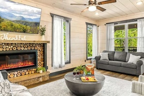 Unwind in a cozy living room featuring a modern fireplace, plush seating, smart TV, and mountain views. Perfect for sipping wine or sharing a charcuterie board by the fire after a day of adventure.
